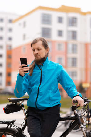 A bearded man is sitting on his bike and using a smartphoneの写真素材