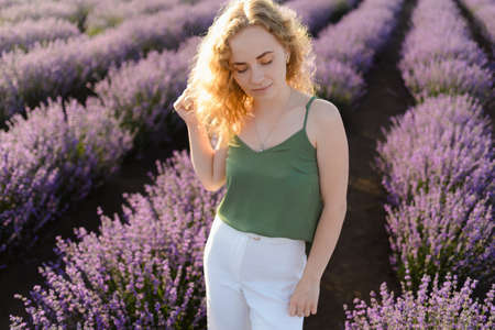 A red-haired woman walks on a lavender field in summer. The woman walking between blossoms of the lavender field at sunsetの写真素材