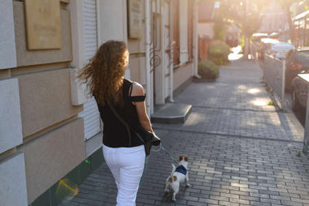 A red-haired woman is walking with her dog on the sidewalk. A daily walk with your petの写真素材