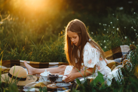 A girl is putting a piece of cake on herself during a picnic in the garden at sunsetの写真素材