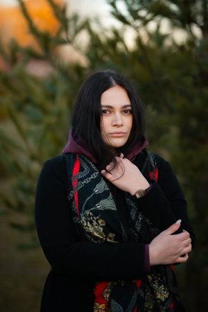 Portrait of a dark-haired girl in the park. The beautiful lady is looking at the camera without a...