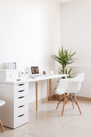 Modern hipster workplace. Small white office with table, chair, notebook and cupの写真素材