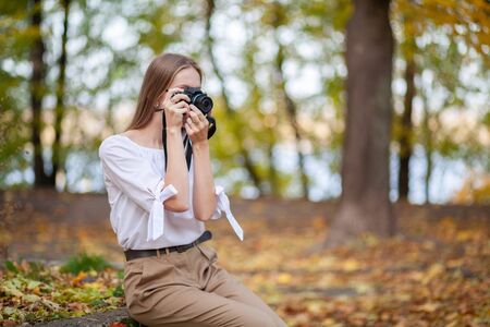 Attractive beautiful young girl holding modern mirror-less camera in autumn park.