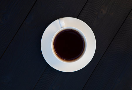 Cup with black tea and saucer on a dark wooden background. View from above.の写真素材