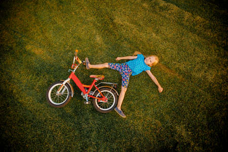 A girl with a bicycle, children with a bicycle, a girl fell off a bicycle, a girl is lying on the grass.の写真素材