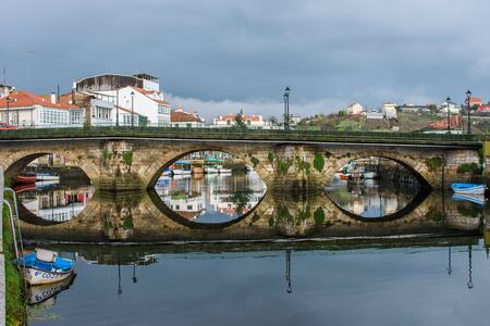 Bridge in a estuary with boats on its sides and reflection in the waterの写真素材