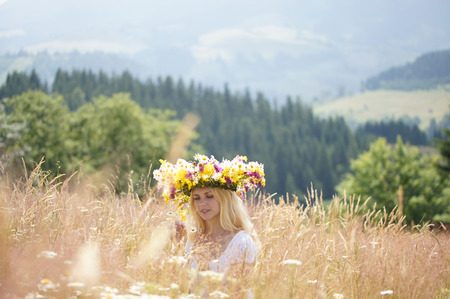 Girl in a wreath on a meadow tells fortunes on a camomileの写真素材