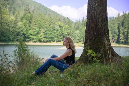 Sad woman sitting near a mountain lake