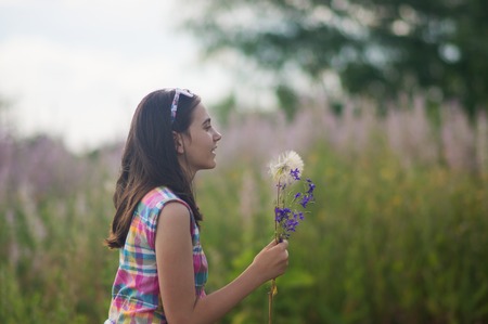 Girl blowing dandelion in the green spring grassの写真素材
