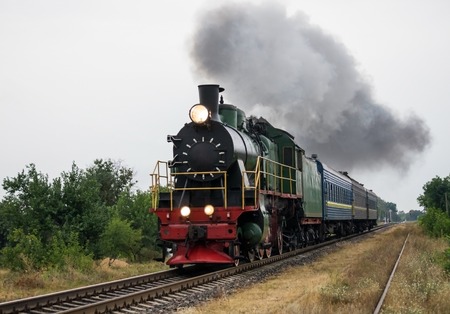 Old steam locomotive travels by rail and produces smoke