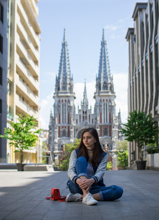 The girl is sitting on the street near the churchの写真素材