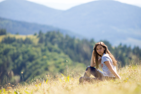 Young girl is sitting on the lawn on the mountainsideの写真素材