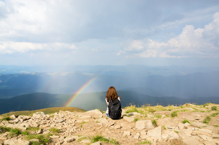 The woman sits in the mountains and looks at the rainbowの写真素材