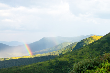 Rainbow and sunlight in the Carpathian mountains over the housesの写真素材