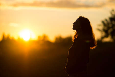 Woman stands with closed eyes at sunsetの写真素材