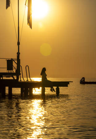 Woman at dawn sitting on the pierの写真素材