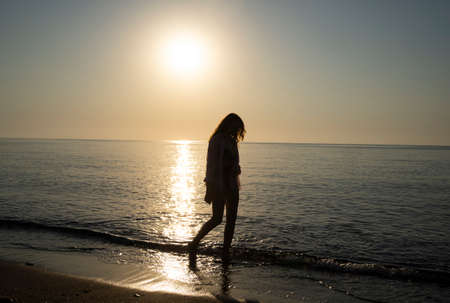 Lonely girl walking along the beach at dawnの写真素材