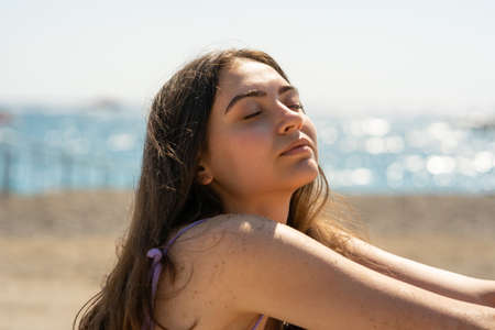 Beautiful girl with closed eyes sits on the seashoreの写真素材