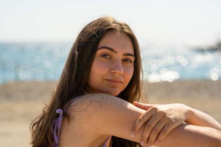 A beautiful girl sits on the seashore with her head turnedの写真素材
