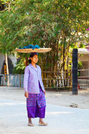 Mandalay, Myanmar - February 28, 2011 : Burmese woman walking on the street and carrying goods in basket placed on her head [description:]Burmese woman walking on the street and carrying goods in basket placed on her headのeditorial素材
