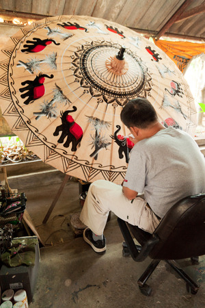 Chiang Mai, Thailand - March 06, 2011: Middle aged artist painting a big umbrella at a workshop in Chiang Maiのeditorial素材