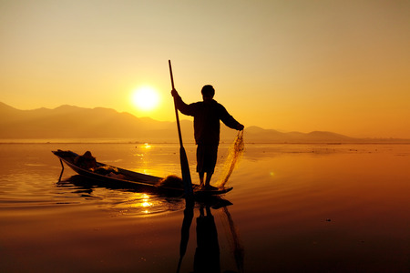 Heho, Myanmar - March 02, 2011 : Intha fisherman fishing at sunset in Inle Lake standing at the end of the canoe.のeditorial素材
