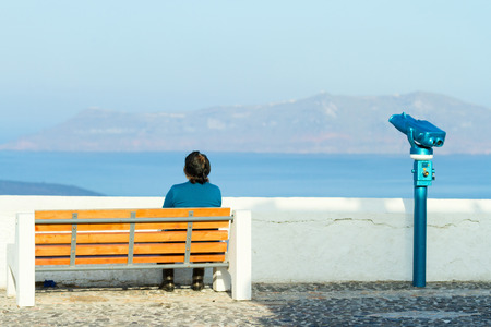 Fira, Greece - May 04, 2012 : Senior greek woman relaxing on a bench with a view to the Volcano early in the morning, before the streets are full with touristsのeditorial素材