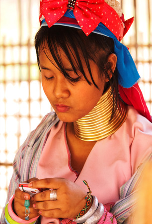 Chian Mai, Thailand - March 07, 2011 : Street portrait of a young long-neck woman writing text messages on cellphone. There are 25 copper rings on her neck weighting 9 kilograms. She has the burden to wear them for life.のeditorial素材