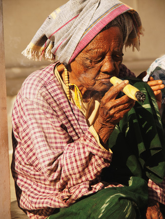 Bagan, Myanmar - February 25, 2011 : Senior Burmese woman smoking handmade cigar inside Shwezigon Pagoda in Baganのeditorial素材