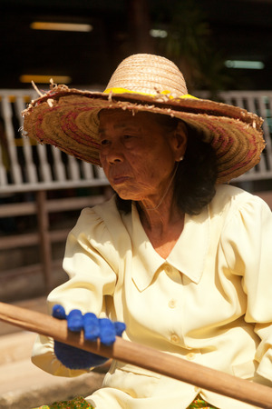 Damnoen Saduak, Thailand - March 21, 2011 : Senior Thai woman with hat selling freshly cooked food and fruits on a boat in Damnoen Saduak Floating Marketのeditorial素材