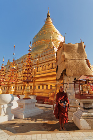 Bagan, Myanmar - February 25, 2011 : Young monk walking barefoot on the ground inside Shwezigon Pagoda carrying his food containerのeditorial素材