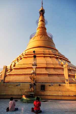 Yangon, Myanmar - February 24, 2011 : Burmese people sitting on the ground and praying in front of Botataung Pagoda in Yangon at sunsetのeditorial素材