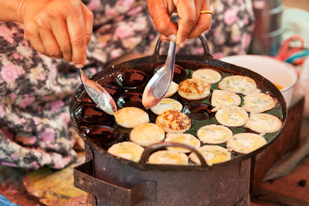 Old Burmese woman cooking street food at five-day market while sitting on the groundの写真素材