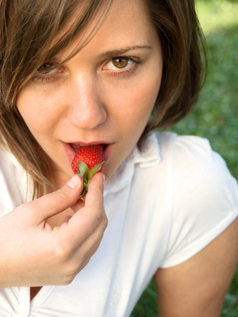 Young woman eating strawberry outdoorsの写真素材
