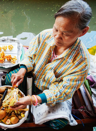 Damnoen Saduak, Thailand - March 21, 2011 : Senior Thai woman selling freshly cooked food and fruits on a boat in Damnoen Saduak Floating Marketのeditorial素材