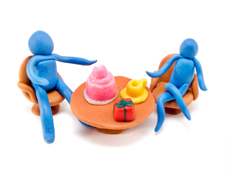 Clay people on a table with a cake, a cup of coffee and a giftの写真素材