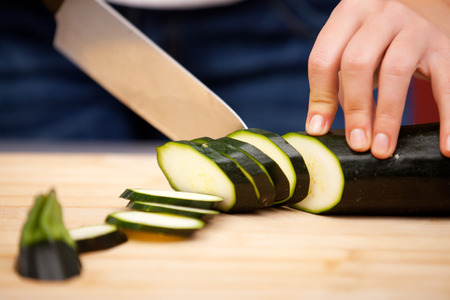 Young woman cutting zucchini in the kitchenの写真素材