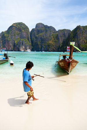 Koh Phi Phi, Thailand - March 15, 2011 - Young Thai man pulling his long-tail boat to the sand on Koh Phi Phi islandのeditorial素材