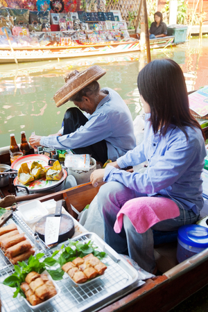 Damnoen Saduak, Thailand - March 21, 2011 : Young Thai woman and a senior Thai Man selling freshly cooked food on a boat in Damnoen Saduak Floating Marketのeditorial素材