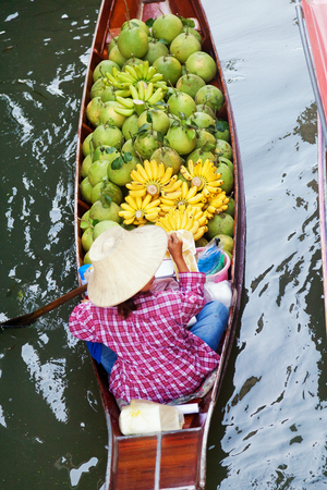 Damnoen Saduak, Thailand - March 21, 2011 : Senior Thai woman with a hat on a boat full of fruits in Damnoen Saduak Floating Marketのeditorial素材