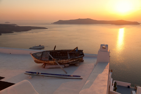 Old boat on the roof of a building in Firostefani, Santorini. Shot at sunset. The volcano on background. Horizontal shotの写真素材