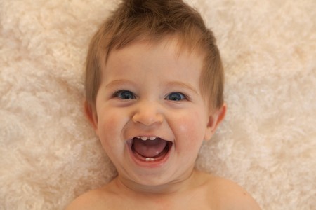 Portrait of a one year old boy with blue eyes and blonde hair. Laying down and laughingの写真素材
