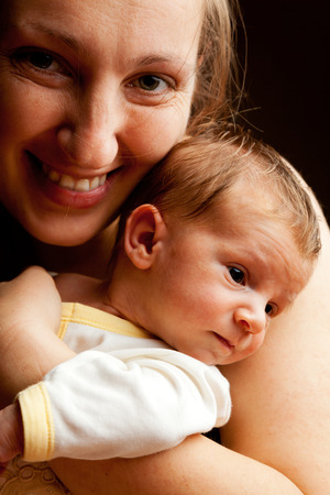 Young mother holding her baby boy and smiling at the camera. Isolated on black backgroundの写真素材