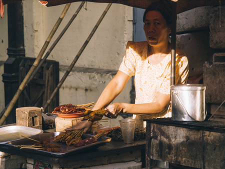 Yangon, Myanmar - February 24, 2011 : Senior Burmese woman selling freshly fried sausages in the street market.のeditorial素材