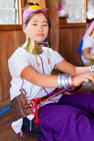 Chian Mai, Thailand - March 02, 2011 : Street portrait of a young long-neck woman weaving in a factory made of bamboo. There are 25 copper rings on her neck weighting 9 kilograms. She has the burden to wear them for life.のeditorial素材