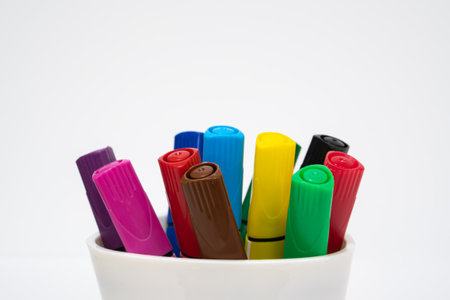Set of multicolored markers in a white cup on white