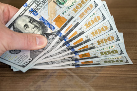 View of a man's hand placing a bundle of 100 dollar bills on a wooden table. Saving money concept