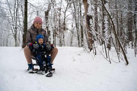 Mother with a child on a sled. A young woman with her little son rides down the hill in a sleigh....