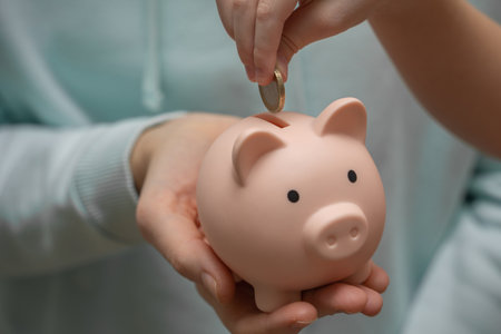 The child puts a coin in the piggy bank that his mother is holding. Saving and accumulating money, financial security, budget planning and investment.の写真素材