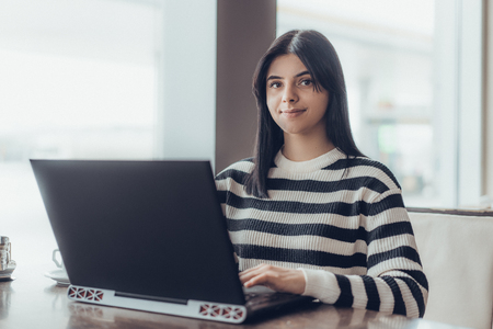 Cropped shot view of young woman keyboarding on laptop computer with blank copy space screen while sitting in cafe, blonde female student working on net-book after her lectures in University,flare sunの写真素材
